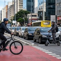Ciclista em bicicleta elétrica e condutor de patinete elétrico na ciclofaixa de uma avenida movimentada