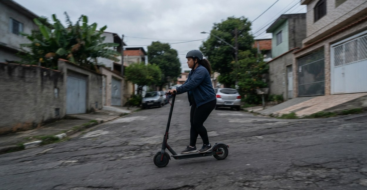 Mulher de capacete sobe uma rua de bairro residencial em pé num patinete elétrico dobrável